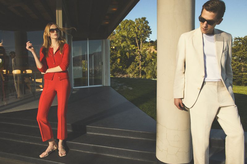 Man in a cream suit and woman in a red outfit standing outside a modern residence.