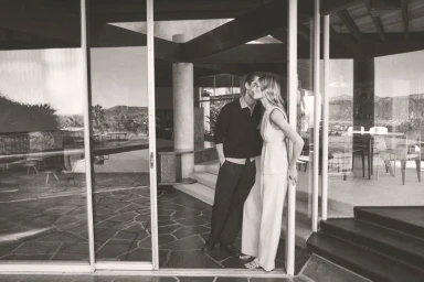 Monochrome image of a man and woman embracing inside a modern glass-walled architectural home for Vince Spring 26.