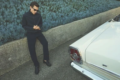 Model Anatol Modzelewski leaning against a stone wall next to a white vintage car for Vince Spring 26 campaign.