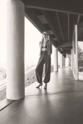 Model standing on a modern outdoor veranda with columns wearing a patterned jacket and dark trousers for Vince Spring 26.