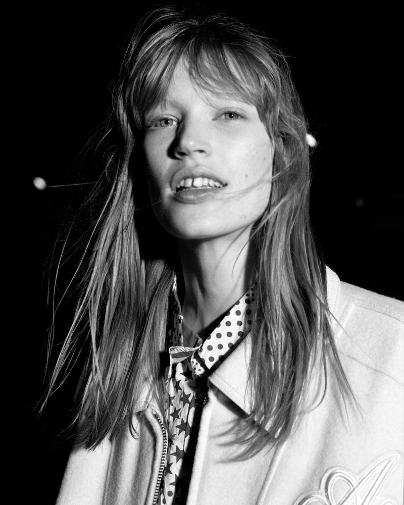 Black and white portrait of a woman with bangs wearing a patterned shirt and light jacket against a dark background
