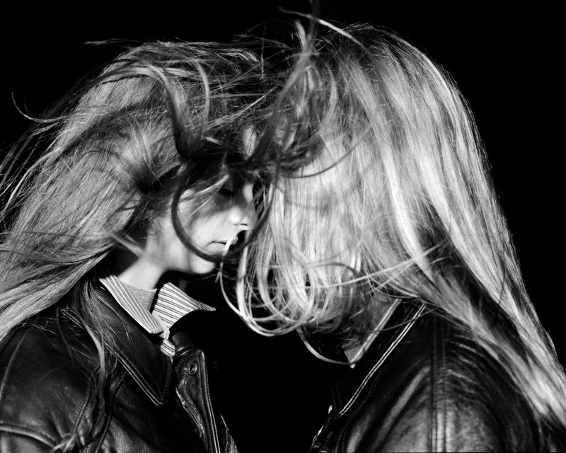 Black and white portrait of two young women with long hair, wearing leather jackets, faces partially obscured by motion.