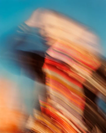Abstract motion-blurred portrait of a person in a colourful patterned top against a bright blue background