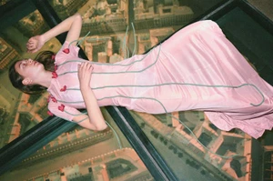 Model lying on glass floor wearing a pink dress with green cord details for Middle Plane Magazine