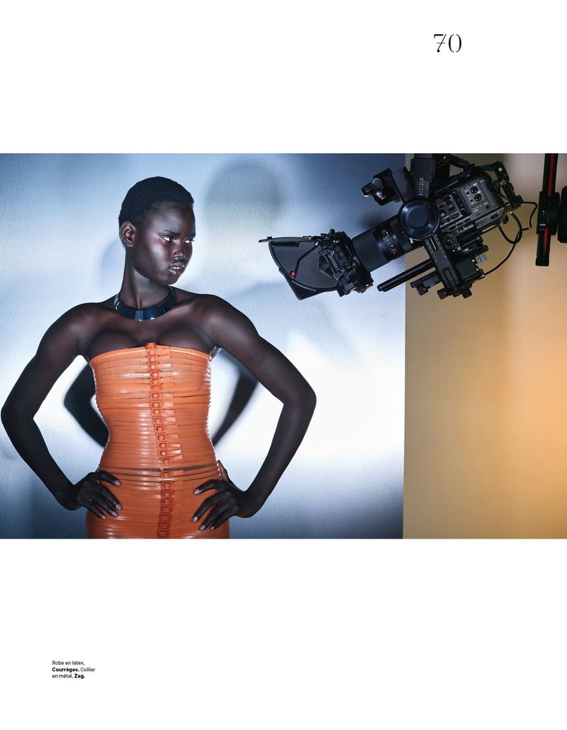Model Nyakong Chan wearing an orange strapless top and dark choker in a studio setting with a professional camera visible