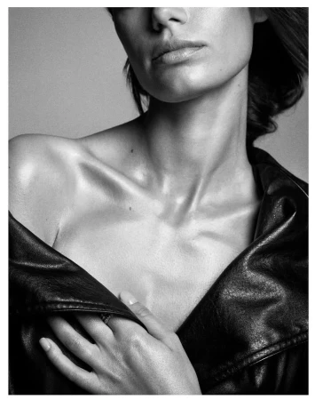 Monochrome portrait of an adult woman wearing a black leather jacket, focusing on her upper body, neck, and hands in a neutral setting.