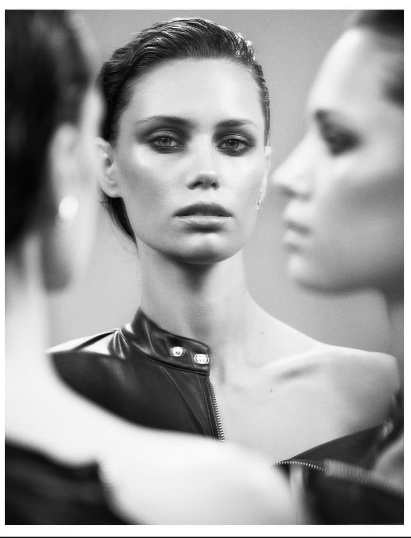 Striking black and white portrait of a woman with slicked-back hair and a black leather jacket, reflected in mirrors.