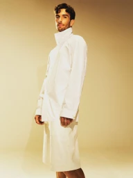 Man wearing a white button-up shirt and shorts standing against a solid beige seamless backdrop.