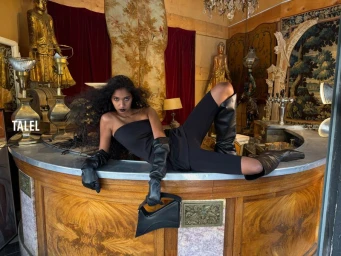 Model wearing black strapless dress and leather boots lying on wooden bar counter