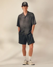 Model wearing a patterned short-sleeve shirt and matching shorts with a cap against a neutral studio backdrop