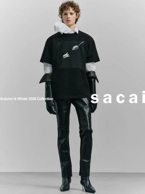 Fashion shot: a slender model in a black tee, glossy black pants, and heels, poses against a gray backdrop with 'sacai' typography.