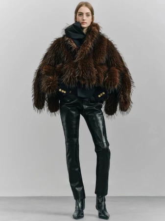 Full-length shot of a model wearing a shaggy brown fur coat with black leather pants and black boots against a neutral backdrop.