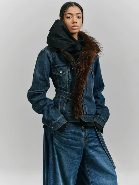 Studio shot of a woman modeling denim jacket with fur collar and wide-leg jeans. She's in a neutral pose against a plain backdrop.