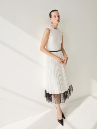 A woman in a white dress and black heels poses against a white wall with shadows, minimalist fashion and style, clean studio lighting.