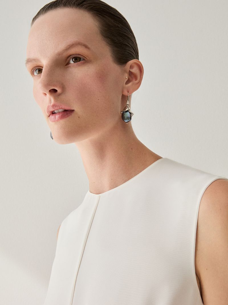 Close-up portrait of a model wearing a white top and dark dangling earrings against a seamless white background