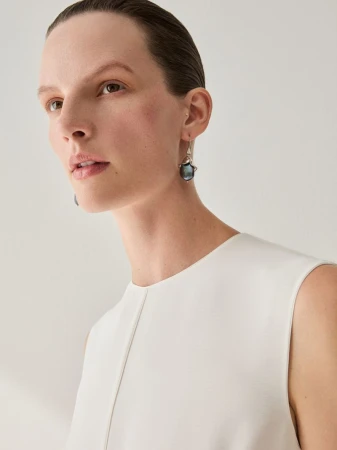 Close-up portrait of a model wearing a white top and dark dangling earrings against a seamless white background