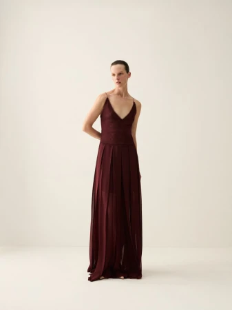 Model Sara Blomqvist wearing a long burgundy pleated gown against a neutral studio background for Giada SS26 pre collection.