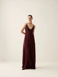 Model Sara Blomqvist wearing a long burgundy pleated gown against a neutral studio background for Giada SS26 pre collection.