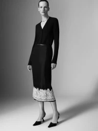 Model Sara Blomqvist wearing a black long-sleeve top and matching midi skirt with white lace hem against a neutral gradient backdrop