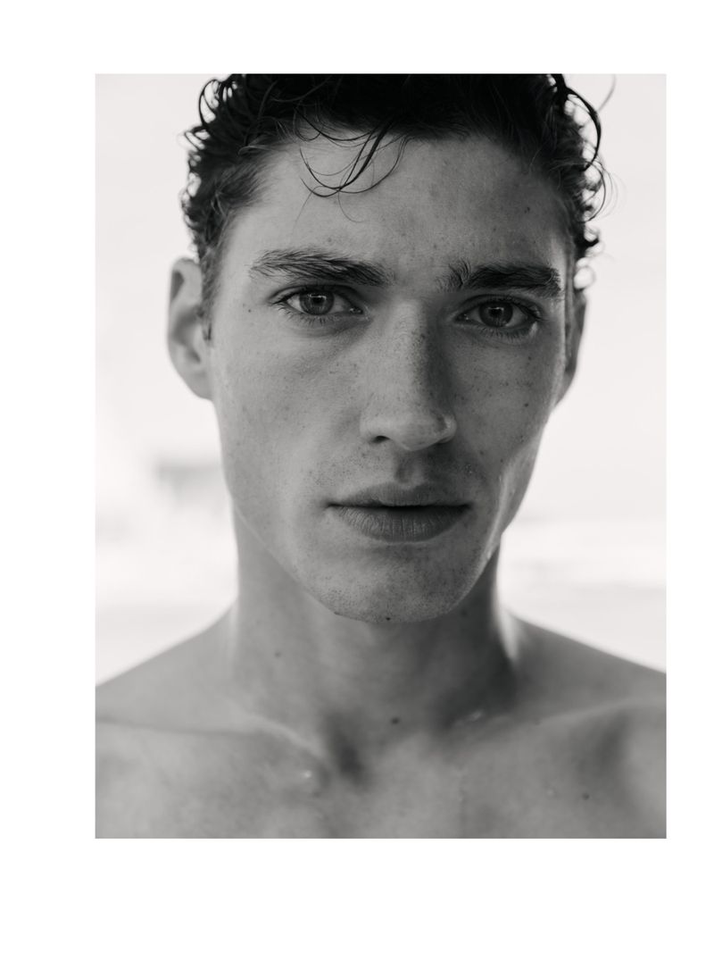 Striking black and white portrait of a young adult man with dark hair, showcasing a close-up of his face with a blurred background.