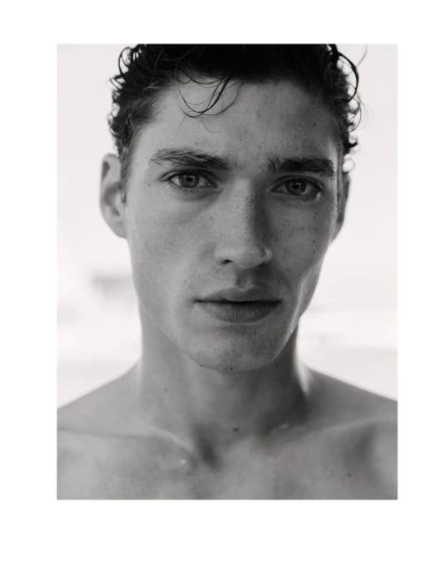 Striking black and white portrait of a young adult man with dark hair, showcasing a close-up of his face with a blurred background.