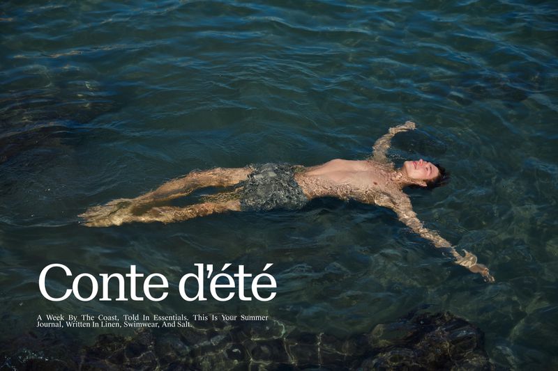 Adult male floats on his back in dark ocean water with arms outstretched and face to the sky in an outdoor fashion editorial.