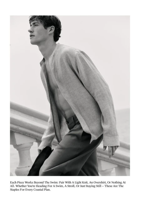 Monochrome fashion shot of a young adult male with fair skin, wearing a light knit shirt and pants, outdoors on a staircase.