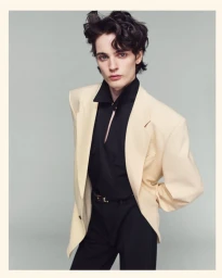 Model wearing an oversized cream blazer over a black button-down shirt against a plain grey studio backdrop
