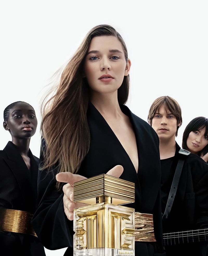 Balmain fragrance bottle held up by a woman with group of diverse people behind her in a beauty and fashion product shot.