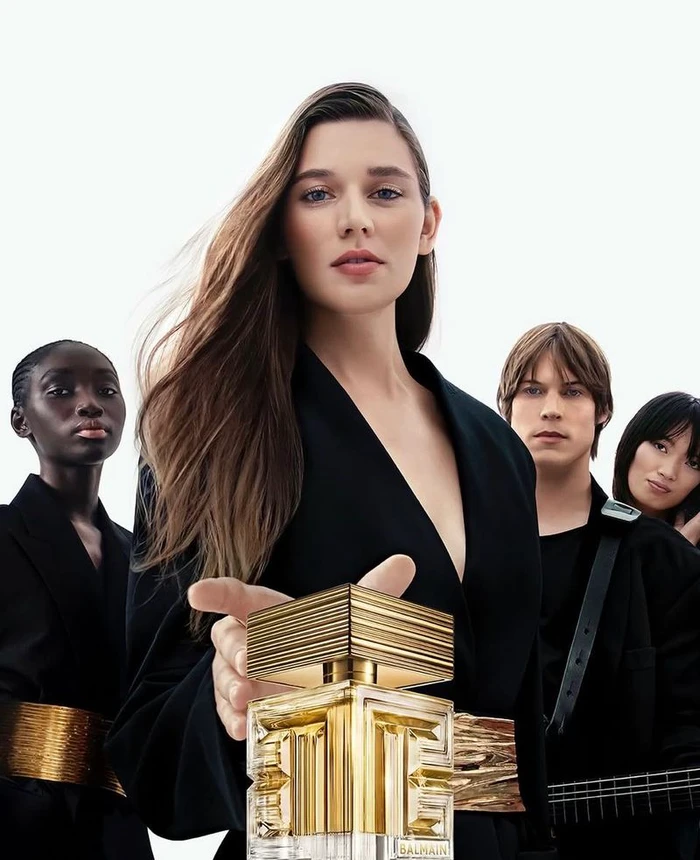 Group of four models in black attire holding a gold perfume bottle for Balmain