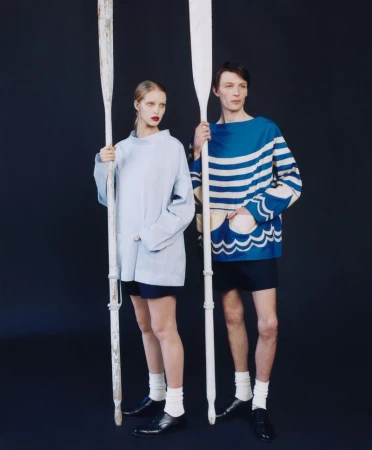 Two models in studio with painted wooden oars, wearing nautical-themed outfits and white socks with shiny black leather shoes against dark backdrop.