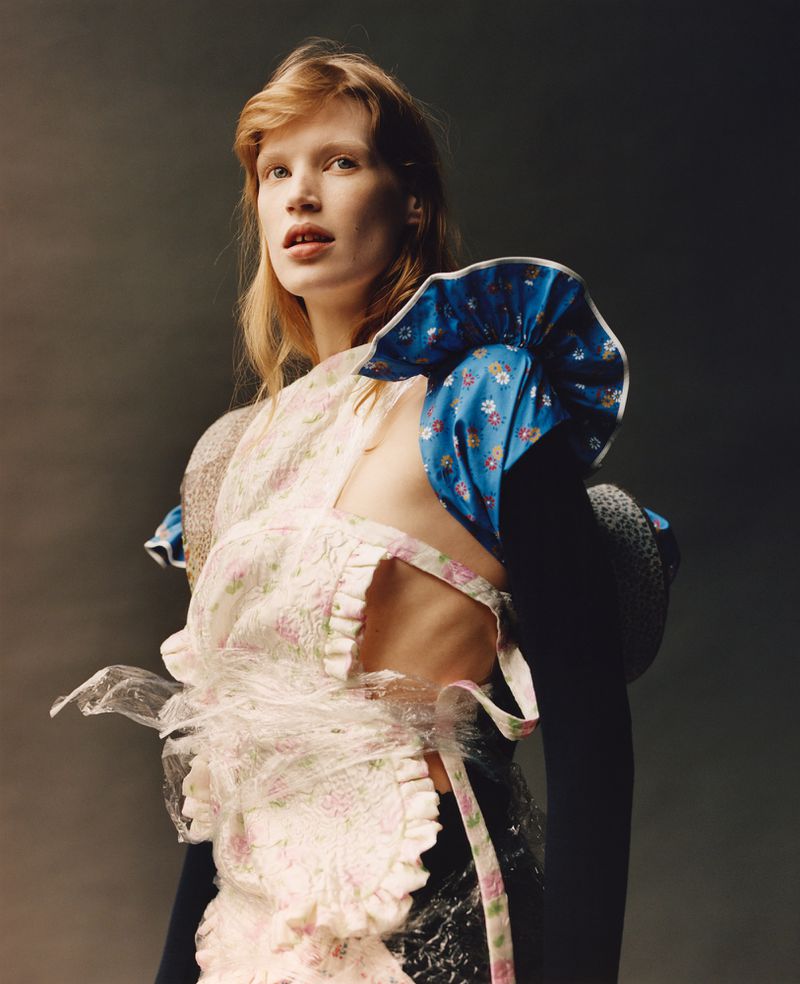Woman in Avant-Garde Fashion Apron and Puffed Sleeves in Studio. Ethereal beauty in unique floral apparel against a grey backdrop.