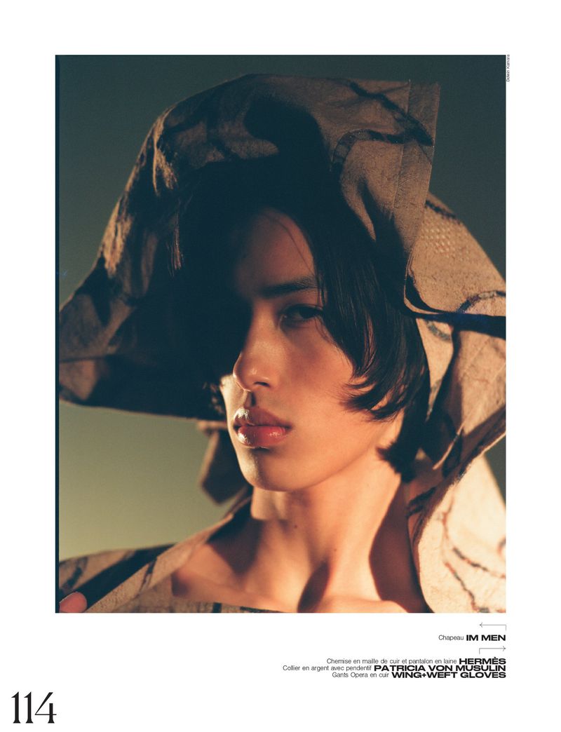 Close-up studio shot of a model wearing a draped taupe hood with neutral makeup and soft lighting, and copy space for editorial use.
