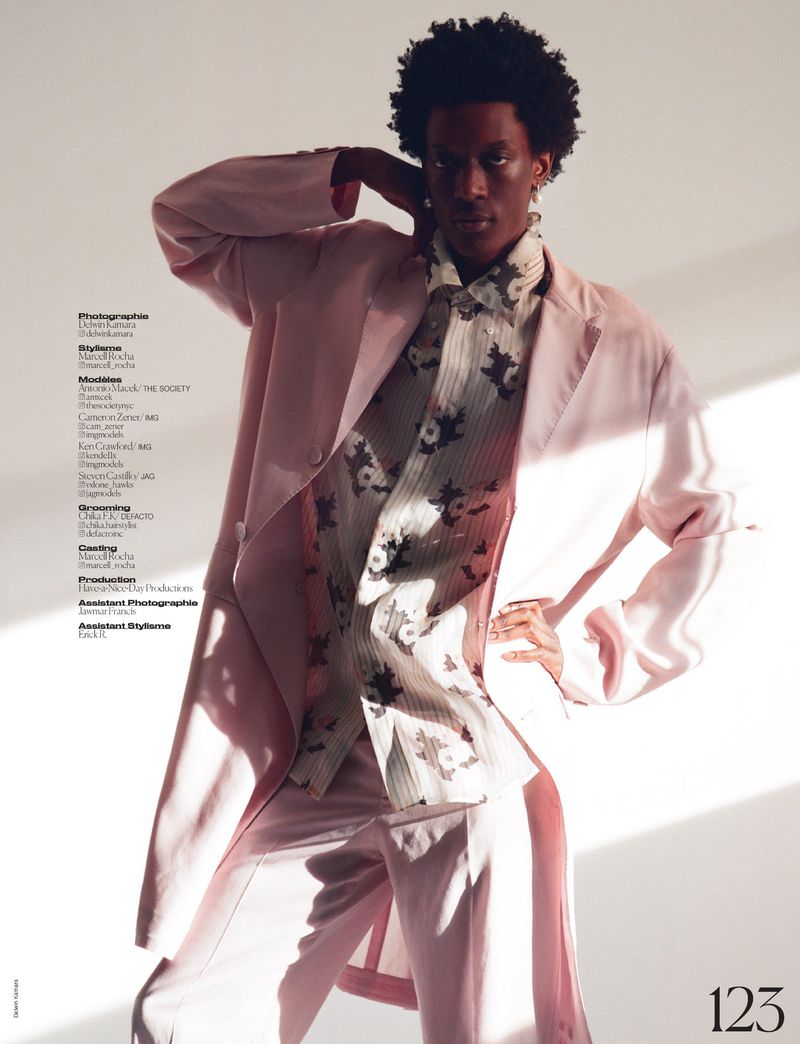 A fashion shot of a slender African-American man in a pink suit with a patterned button-down shirt in a softly lit photo studio.