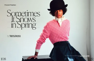 Model wearing a pink cable knit sweater and black bowler hat leaning against a dark surface for French Magazine editorial.