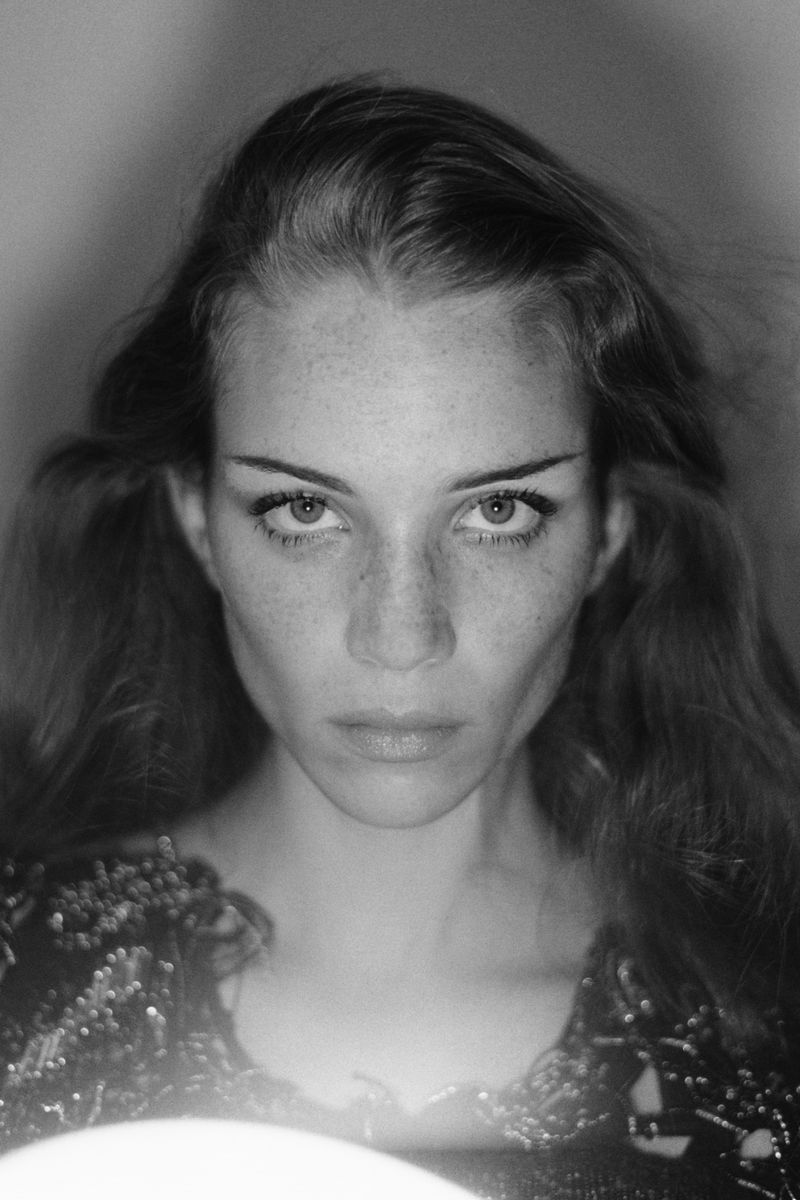 Portrait of a fair-skinned woman with freckles, captured in a black and white photograph, wearing a beaded top and looking directly at the camera.