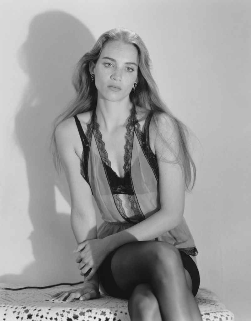 Model Rebecca Leigh Longendyke in a black lace top seated against a plain background for Self Service.