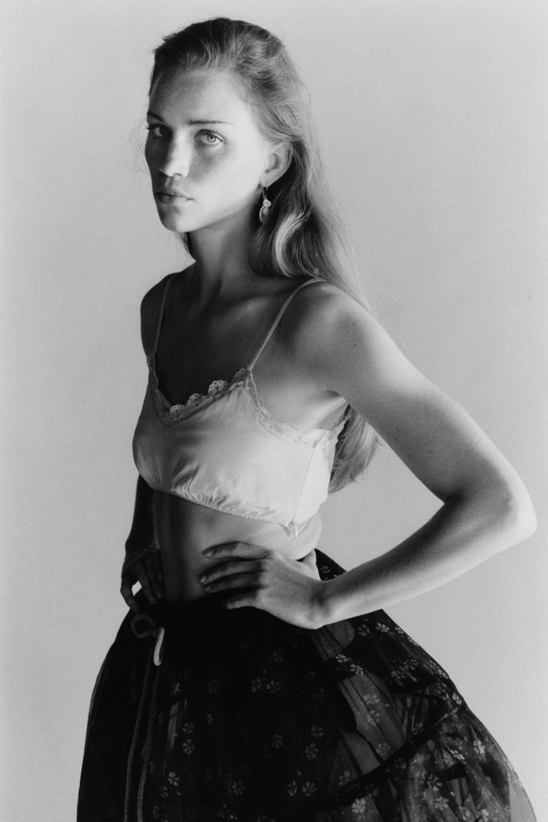 Monochrome portrait of a young woman in a strappy crop top and a floral skirt posing with her hands on her waist in a studio.
