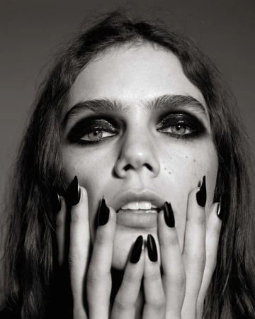 Close-up portrait of a model with dramatic dark eye makeup and long black nails framing her face for Self Service by Alasdair McLellan.