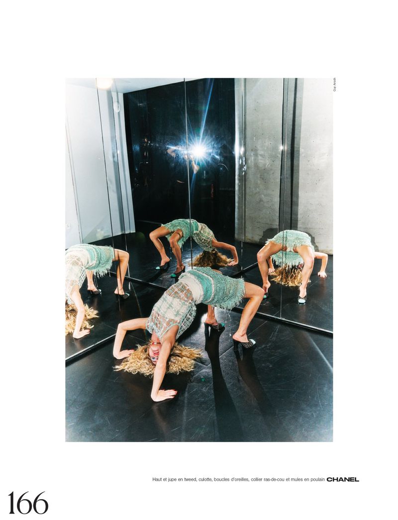 A woman in a light green dress does a backbend on a shiny black floor, reflected in mirrored walls in a studio setting.