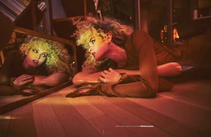 Model Morgan Fletcher with curly blonde hair lying on a wooden floor, reflected in a mirror under warm ambient lighting for French Magazine.