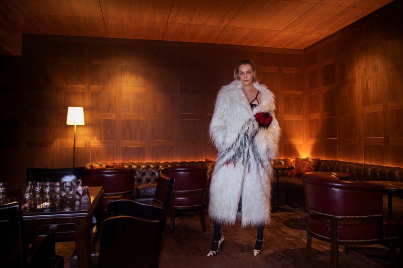 Fashion shot of a woman in a white faux fur coat with a dark interior background, showcasing elegant apparel and classic styling.