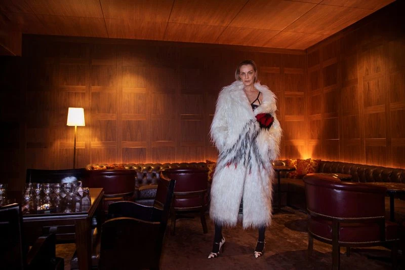 Fashion shot of a woman in a white faux fur coat with a dark interior background, showcasing elegant apparel and classic styling.