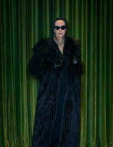 Model Simonetta Gianfelici wearing a black faux fur coat and sunglasses against green velvet curtains for Numéro Switzerland.