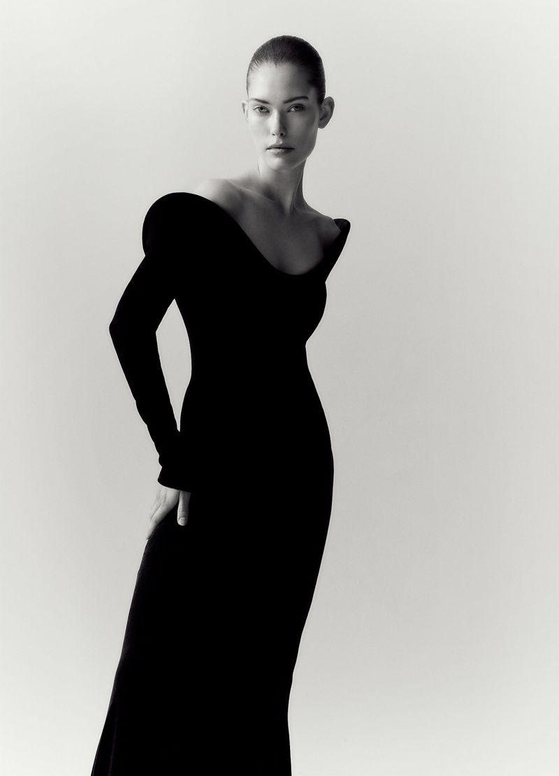 Elegant full-length portrait of a female model in a fitted black gown against a bright white background. Fashion editorial style.