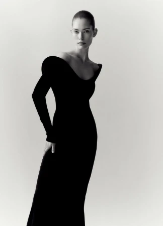 Elegant full-length portrait of a female model in a fitted black gown against a bright white background. Fashion editorial style.