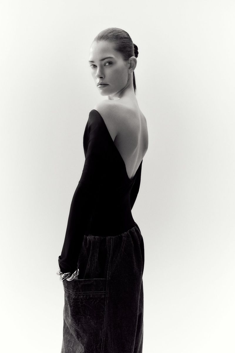 Monochrome portrait of a woman in a low-back top and loose jeans, turned to the side, with a bright background.