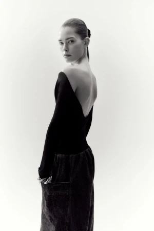 Model wearing a black long-sleeve top and dark trousers against a white seamless background for Net-A-Porter.