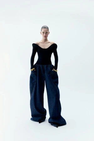 Model wearing a fitted black off-the-shoulder top and wide blue denim trousers against a white seamless background.