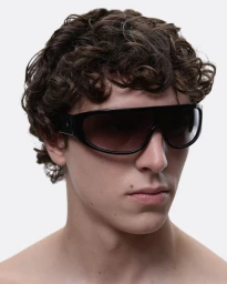 Portrait of a man with dark curly hair wearing thick black sunglasses against a white background